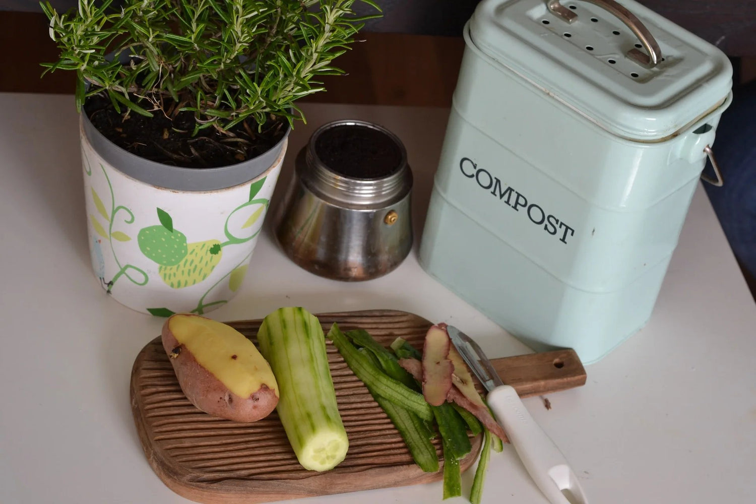 veggies on cutting board with rosemary plant and small compost bin